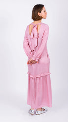 Woman wearing a pink dress with long sleeves and a bow detail on a white background